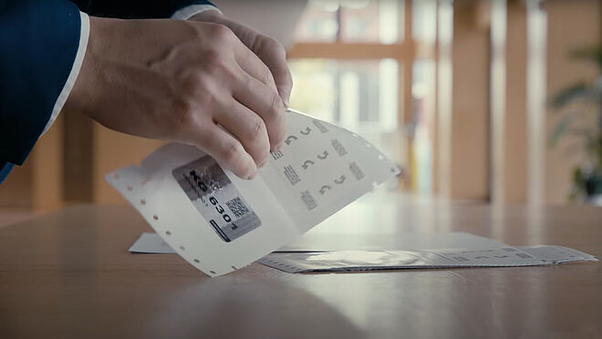 Imagen de manos tirando de una etiqueta adhesiva de KINEGRAM de su sustrato de papel para aplicarla en una superficie