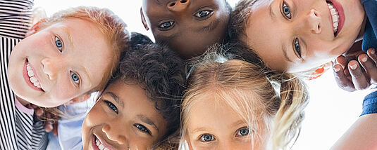 Image of smiling children's faces in a circle, looking down at the camera.