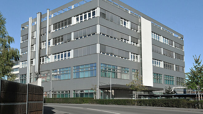 Imagen de la sede y planta de producción de OVD Kinegram en Zug (Suiza), un moderno edificio de siete plantas con fachada plateada.